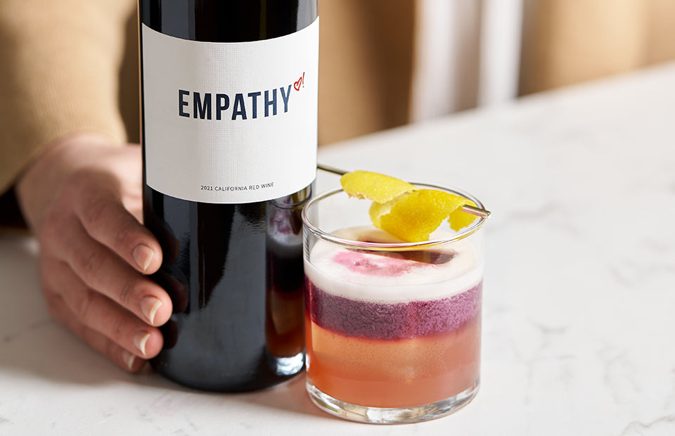 Bottle of Empathy red wine next to cocktail.