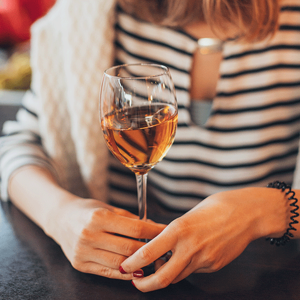 A woman in a striped shirt holds a glass of rose wine. 